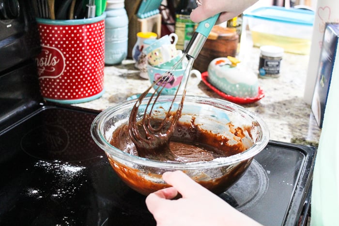 Whisking chocolate batter in a glass bowl next to a red tin